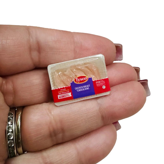 Hand holding a small package of chicken breasts against a white background