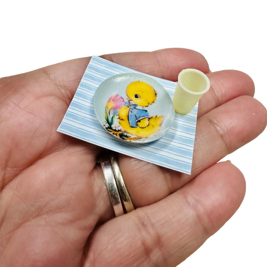 Hand holding a small duck plate and cup on a place mat.
