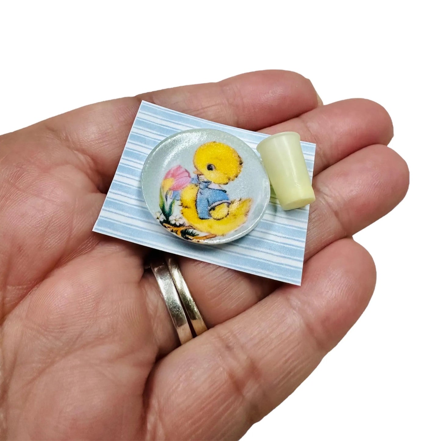 Hand holding a small duck plate and cup on a place mat.