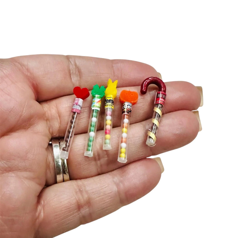 Hand holding five small, colorful candy-shaped items against a white background