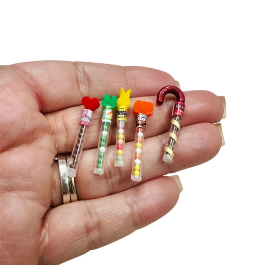 Hand holding five small, colorful candy-shaped items against a white background