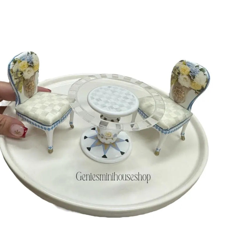 Miniature table and chairs set on a white platform with floral designs, brand 'Gentesminihouseshop' visible.