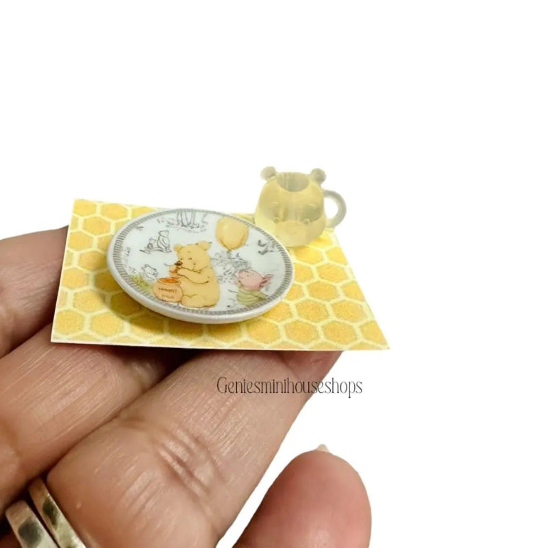 Miniature plate and mug of bear yellow honeycomb background held by a hand.