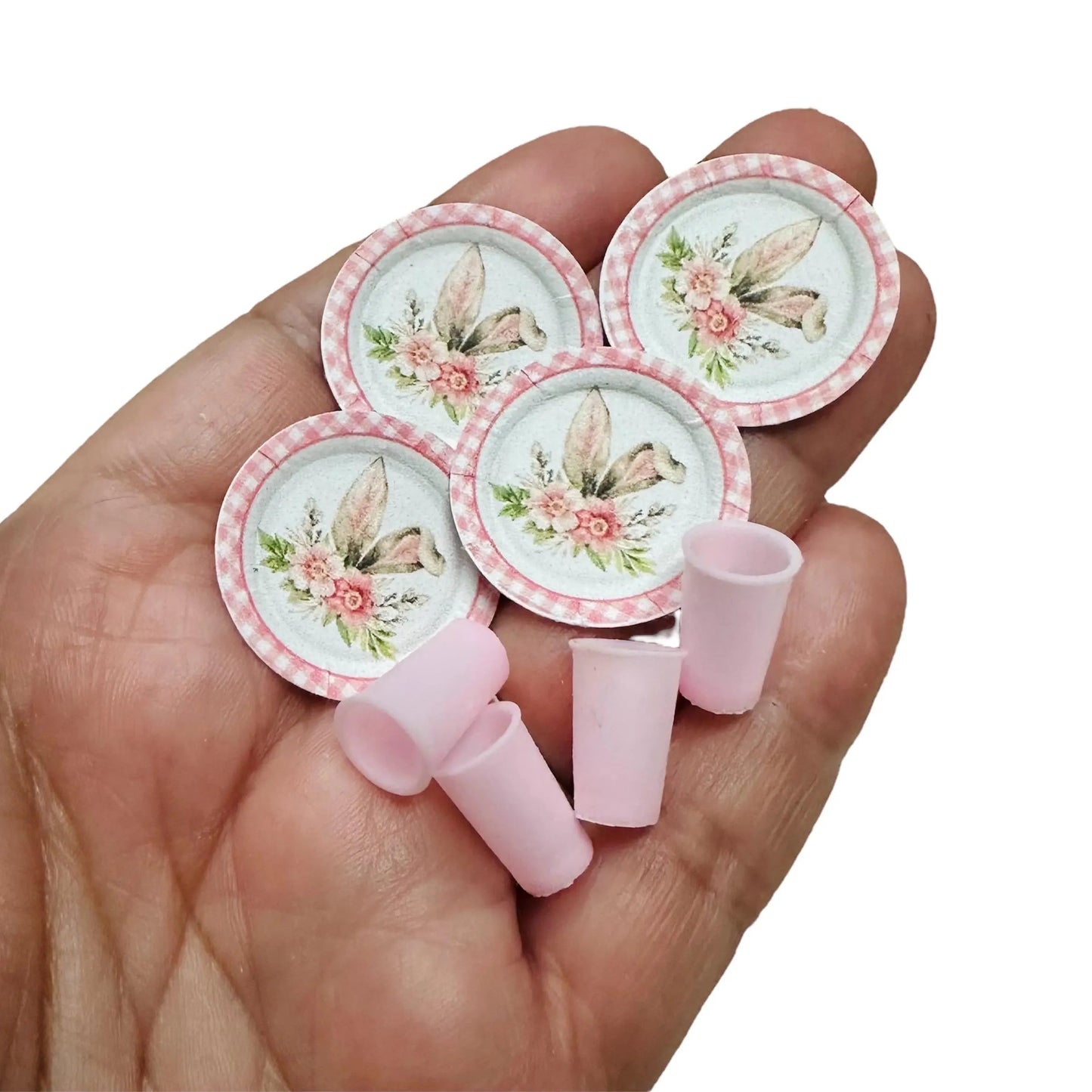 Set of miniature floral plates and cups held in a hand on a white background