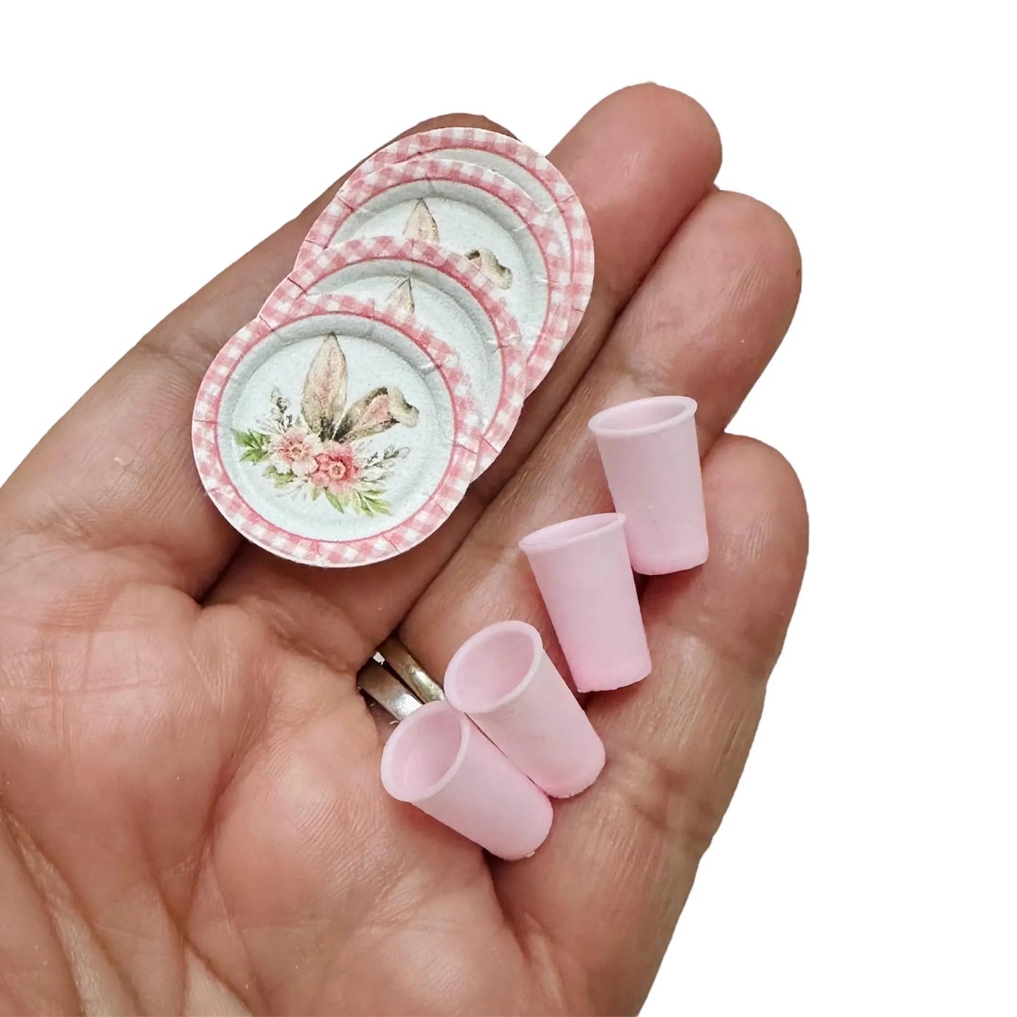 Set of miniature floral plates and cups held in a hand on a white background