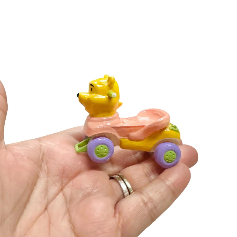 Toy figure of a bear in a pink car held in a hand on a white background