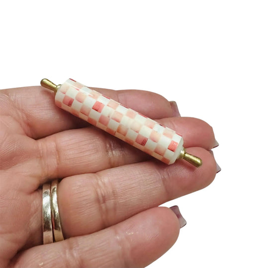Hand holding a small pink rolling pin with a checkered pattern on a white background