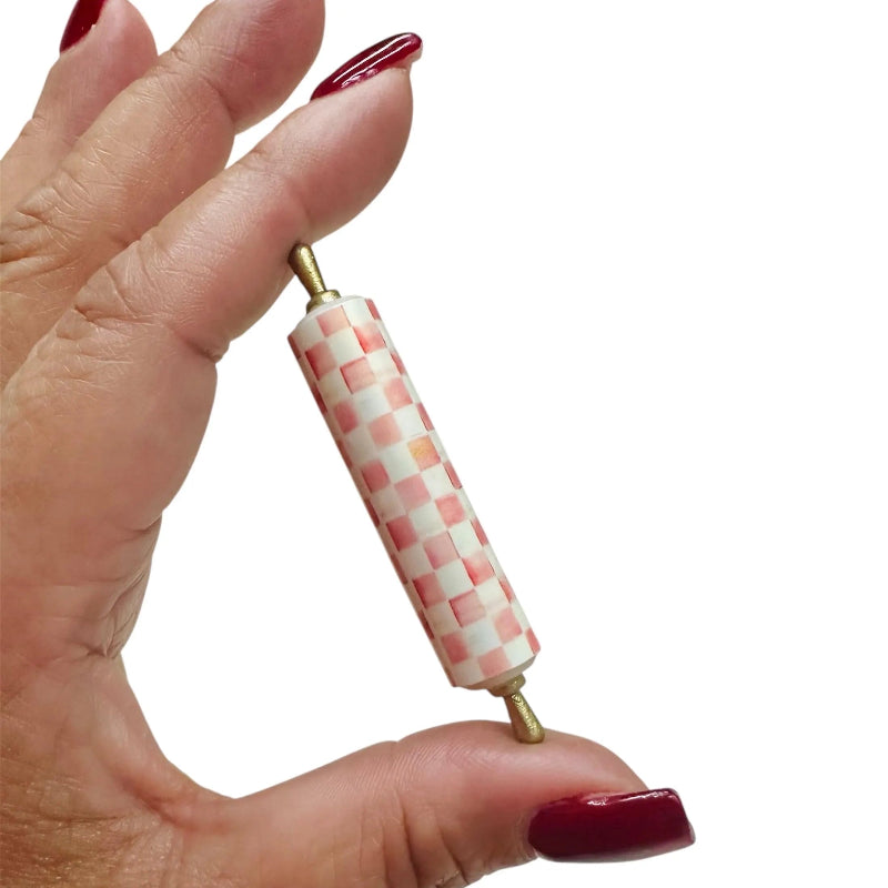 Hand holding a small checkered rolling pin against a white background